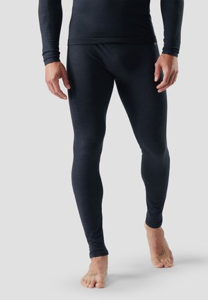 Mand iført sorte tætsiddende lange underbukser og trøje, stående barfodet på lysegrå baggrund.