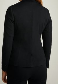 Schwarz taillierter Blazer mit Reverskragen, figurschmeichelndem Design, langen Ärmeln und Zwei-Knopf-Manschetten. Glattes Material und dezente Rückennaht.