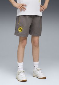 Grå sportshorts med gula accenter och BVB-logotyp. Bärs med vita sneakers och ribbad vita strumpor. Slät tyg, knälång design.