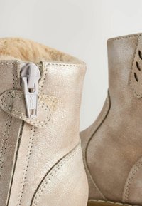 Metalliska silverfärgade anklarboots med en texturerad yta, som har en sidodragkedja och fuskpälsfoder upptill. Detaljerad sömnadsaccent.