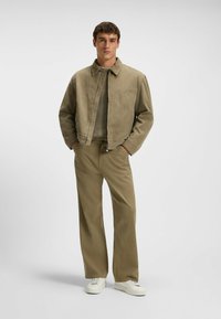 Giacca di velluto a coste beige con colletto, abbinata a pantaloni larghi coordinati e sneakers bianche. Camicia in maglia con texture sotto.