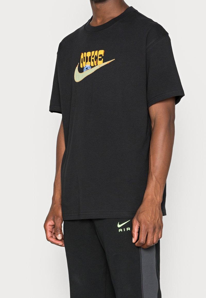 Svart bomulls t-shirt med en färgglad Nike-logotypdesign i orange, grön och blåa nyanser. Kort ärm och avslappnad passform.