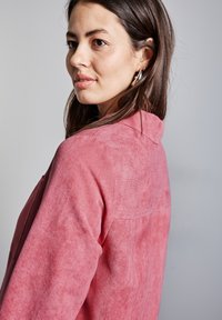 Vaaleanpunainen korduroy-paita, jossa on kaulukset, lämpimästi ribattu pinta, pitkät hihat ja näkyvät saumat. Malli seisoo hieman sivuttain.