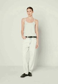 Top branco sem mangas com alças finas, combinado com jeans largos de um azul claro e um cinto preto, complementado com mocassins pretos. Look simples e casual.