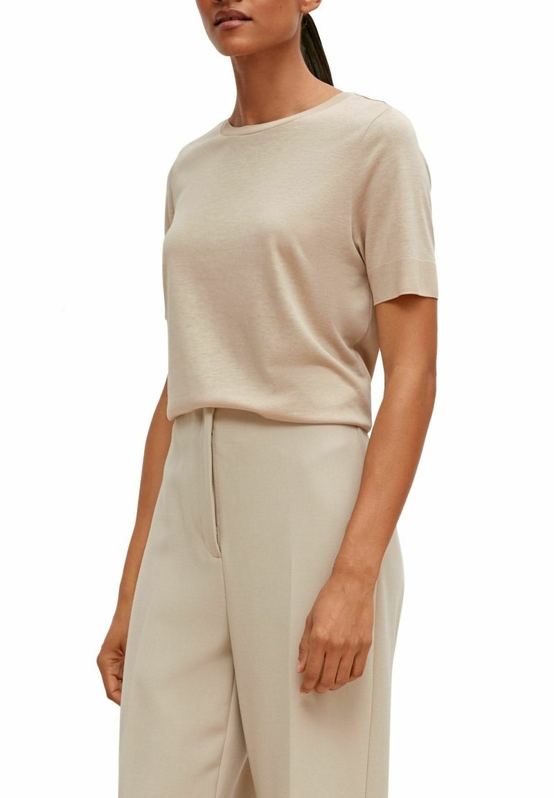 Haut beige à manches courtes avec un col rond, fabriqué à partir d'un tissu doux et lisse. Associé à un pantalon taille haute assorti.