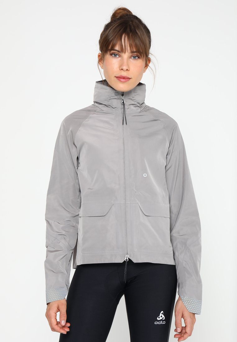 Hellgraue wasserdichte Jacke mit hohem Kragen, Frontreißverschluss, zwei Fronttaschen und gepunkteten Akzenten an den Ärmeln. Ideal für Outdoor-Aktivitäten.