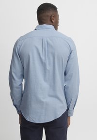 Light blue button-up shirt with long sleeves, back yoke, curved hem, and buttoned cuffs, made from a textured fabric.