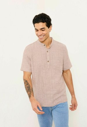 Short-sleeve, light pink linen shirt with a stand collar, three-button placket, and a chest pocket, paired with blue denim jeans.