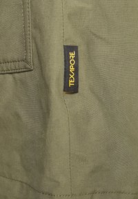 Olive green fabric with visible stitching and texture, featuring a black and yellow "TEXAPORE" label on the side.