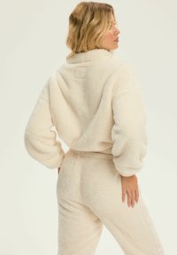 Zestaw dresowy z polaru w odcieniu kremowym, składający się z krótkiej, oversize'owej kurtki o miękkiej teksturze i elastycznych mankietach, w połączeniu z pasującymi spodniami.