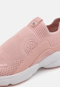 Gros plan d'une basket rose à enfiler en tissu tricoté, semelle texturée et logo MK embossé sur le côté.