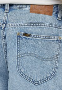 Vaaleansiniset farkut, joissa on erottuva takatasku mustalla "Lee"-tunnuksella. Rakeinen kangas ja nahkainen vyötäröliimattu.