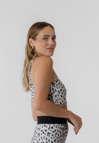 Športová podprsenka s leopardím vzorom a zodpovedajúce legíny s čiernym elastickým pásom; mäkký, pružný materiál; priliehavý strih; bočný pohľad.