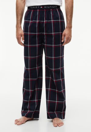 Męskie granatowe spodnie do piżamy w kratę z czerwonymi i białymi liniami, elastyczny pas z logo Tommy Hilfiger, noszone boso.
