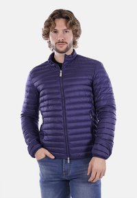 Giacca a vento viola con texture trapuntata, colletto alto e cuciture verticali. Presenta una zip centrale e due tasche laterali.