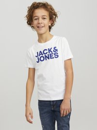 Camiseta de algodón blanca con el texto en azul "JACK & JONES" en un diseño atrevido. Combinada con jeans azules, que muestran un ajuste y textura casuales.