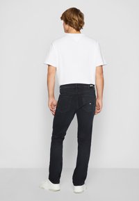Jeans de mezclilla negra con corte slim, combinados con una camiseta blanca de algodón. Características notables incluyen bolsillos traseros y una etiqueta de la marca.