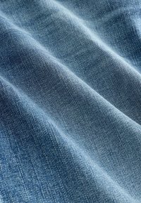 Jasnoniebieski materiał dżinsowy o miękkiej, teksturowanej powierzchni, z diagonalnym splotem i subtelnymi różnicami w kolorze i odcieniu.