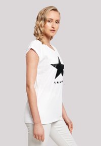 White cotton t-shirt featuring a large black star graphic and small black accents below. Short sleeves and a round neckline.