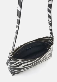 Schwarz-weiße Zebra-Print-Handtasche mit Reißverschluss, verstellbarem Riemen und weicher Innenauskleidung. Verfügt über eine schlanke, längliche Form.