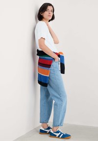 Un tricou alb, blugi albaștri cu talie înaltă și adidași albaștri cu dungi albe. Un cardigan tricotat multicolor legat la talie.