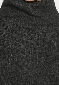 Maglione a collo alto grigio scuro con una texture a coste e materiale in maglia morbida, dotato di un colletto alto e cuciture minimali visibili.