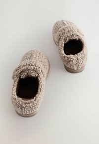 Et par beige fuzzy sutsko med tekstureret stof og runde tæer på en hvid baggrund.