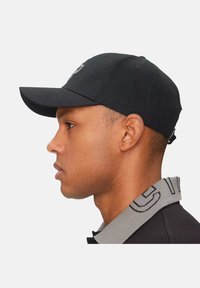 Gorra de béisbol negra con visera curveada y tela texturizada, mostrada en una persona. Con un logo en la parte frontal.