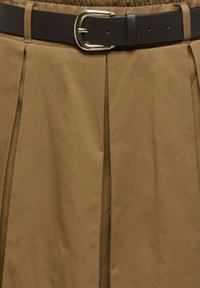 Jupe plissée marron avec une ceinture noire ornée d'une boucle argentée à la taille.
