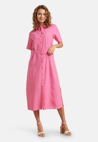 Rosa Hemdblusenkleid mit kurzen Ärmeln, tailliert mit Gürtel und seitlichen Schlitzen, aus leichtem Stoff mit glatter Textur.