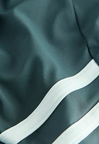 Tekstureret turkis stof med hvide accentriber, glat og let med en subtil glans. Syningerne er pæne og sikre.