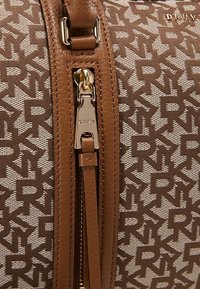 Brązowa torebka z wzorem, wykonana z teksturowanej tkaniny z skórzanymi akcentami, z wyraźnym zamkiem błyskawicznym i metalowymi elementami.