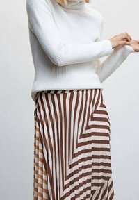 Maglione bianco a collo alto abbinato a una gonna plissettata con strisce zigzag marroni e crema di larghezze variabili.