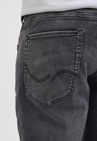 Jeans din denim gri, cu un buzunar la spate cu un model minimalist de cusătură curbată. Țesătura are o textură moale și un aspect ușor decolorat.