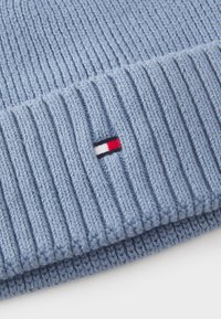 Lichtblauwe gebreide beanie met een geribbeld textuur. Heeft een klein geborduurd logo in rood, wit en blauw aan de zijkant. Zacht materiaal.