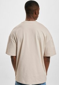 T-shirt oversize beige, maniche corte, in morbido cotone. Design semplice con scollatura rotonda, senza pattern o decorazioni visibili.