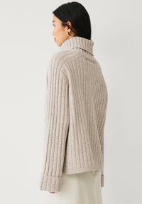 Beige gerippter Pullover mit hohem Kragen, strukturiert für bessere Sichtbarkeit. Verfügt über lange Ärmel und eine lockere Passform, gefertigt aus weichem Material.
