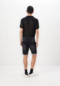 Black mesh short-sleeve shirt with a textured pattern, paired with dark denim shorts featuring rolled cuffs and a five-pocket design. White sneakers.