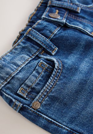 Jeans aus Denim mit bläulichem Farbton, kontrastierenden goldenen Nähten, mehreren Taschen und einem Metalldruckknopf. Weiche Textur.