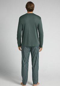 Tmavě tyrkysový top s dlouhým rukávem a pruhované pyžamové kalhoty v modré a bílé barvě. Měkká tkanina, uvolněný střih a žádné viditelné ozdoby.