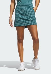 Spódnica w zielononiebieską kratę gingham z elastycznym pasem, dwoma bocznymi kieszeniami i długością do kolan, zestawiona z białymi butami sportowymi.