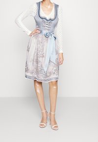 Jasnoniebieski dirndl z dopasowaną górą z sznurowaniem, prześwitującą bluzką z długimi rękawami oraz haftowaną spódnicą z satynowym wiązaniem.