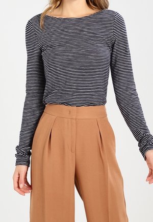 Femme portant un haut à manches longues rayé horizontal noir et blanc rentré dans un pantalon large taille haute couleur beige.