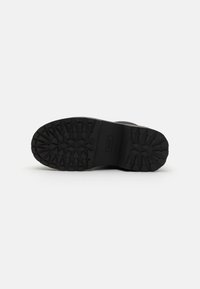 Semelle de botte en caoutchouc noir avec un motif de semelle texturé, comprenant de profondes rainures pour une meilleure adhérence et le nom de la marque embossé au centre.