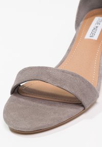 Sandale à bout ouvert en suède gris avec une bride unique sur les orteils et une semelle intérieure rembourrée beige avec une couture visible.