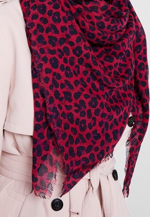 Écharpe rouge ornée d'un imprimé léopard noir, tissu léger avec bords effilochés, drapée autour du cou par-dessus un trench-coat clair.