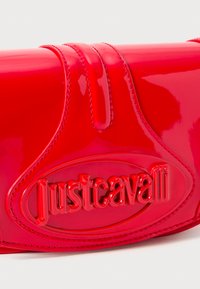 Glossy red clutch bag with embossed "Just Cavalli" logo in raised lettering on front panel.