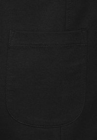 Czarna tkanina z widoczną kieszenią o zaokrąglonych rogach i przeszytymi brzegami, prezentująca gładką teksturę i prosty design.