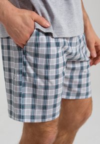 Spodnie szorty w kratę w kolorze białym, szarym i turkusowym. Wykonane z lekkiego materiału, z elastycznym paskiem w talii i bocznymi kieszeniami. Gładka tekstura.