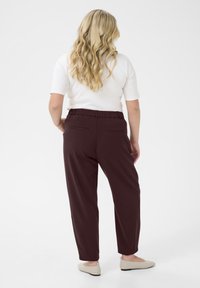Maroon tapered pants with an elastic waistband and back pockets, paired with cream flats, displayed from the back. Smooth fabric texture.